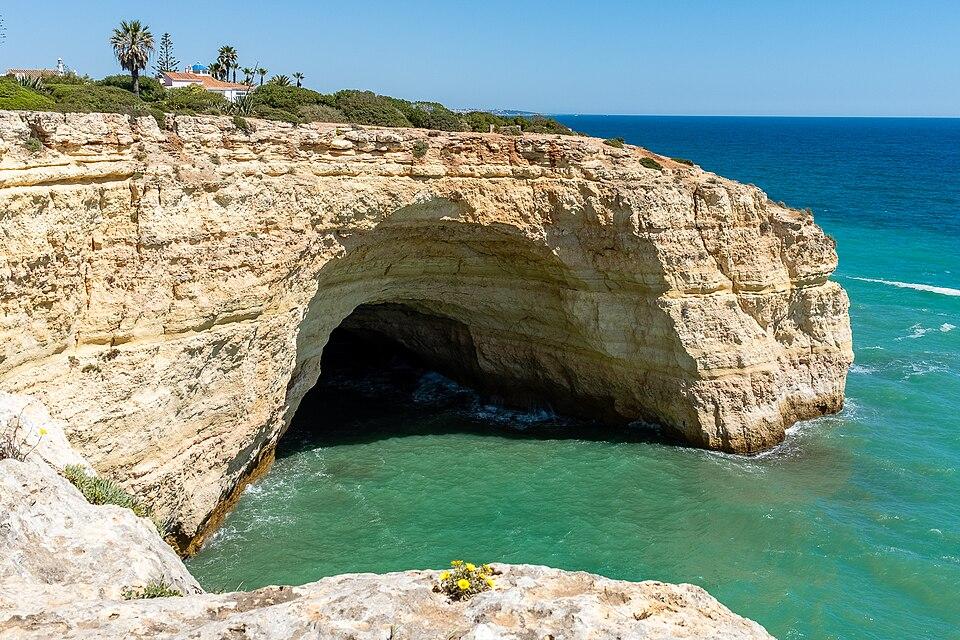 Paddleboarding nära Benagil Cave i Algarve, Portugal, med turkost vatten, solljus genom grottkupolen och en liten båt inuti.