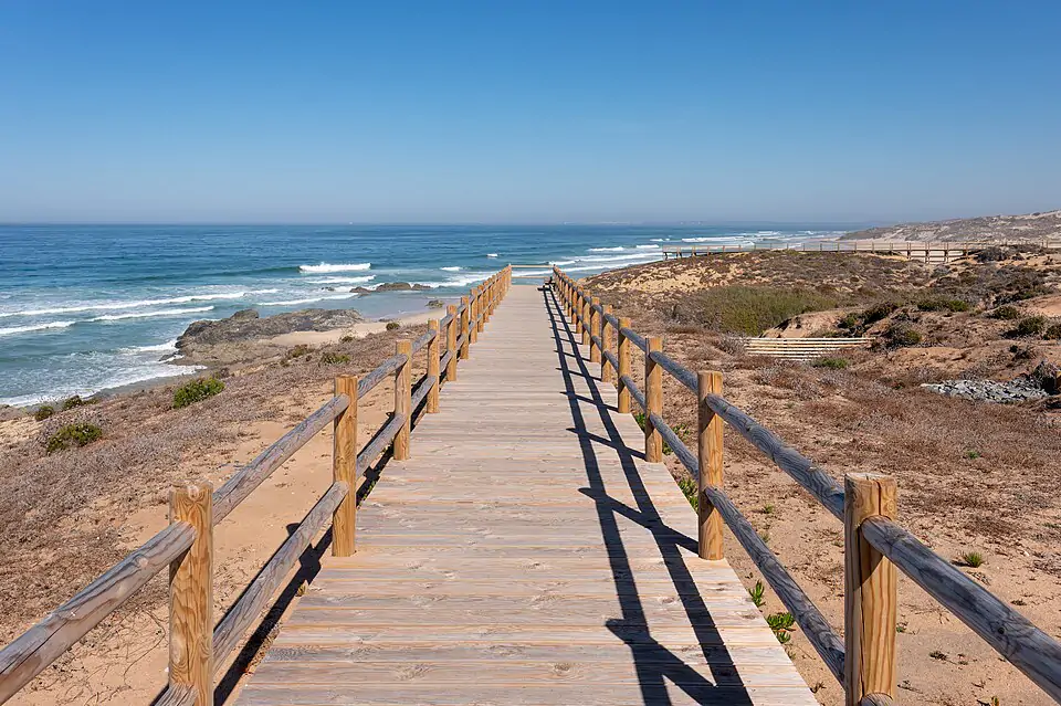 Träpromenaden vid Malhão-stranden med utsikt över den vidsträckta sandstranden och de rena vågorna - en vild surfplats i Alentejo.