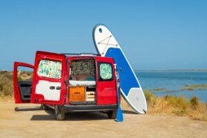 A paddleboard and a red campervan parked by the Algarve coast, Ocean Camper equipment for paddleboarding adventures in Portugal.