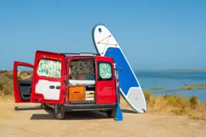 En paddleboard och en röd campervan parkerade vid Algarvekusten, utrustning från Ocean Camper för paddleboard-äventyr i Portugal.