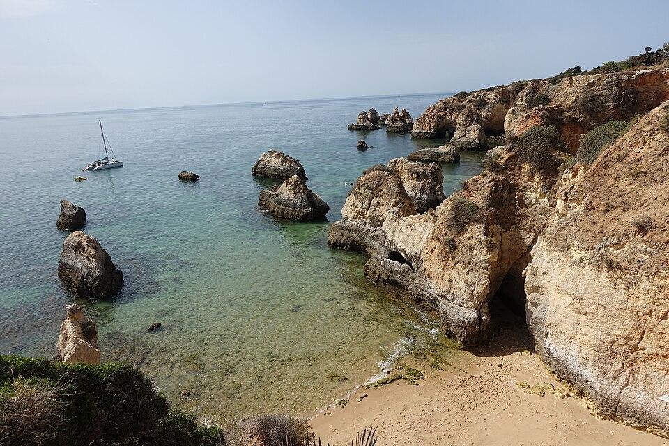 Playa do Alemão en Alvor, Algarve, Portugal - acantilados dorados, agua turquesa y formaciones rocosas con un velero frente a la costa.