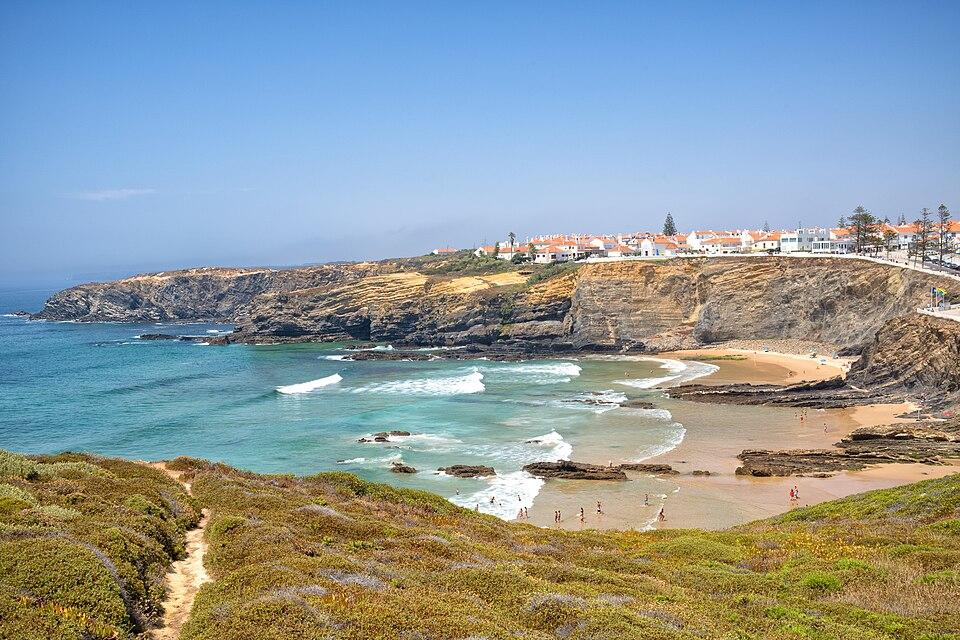 La spiaggia di Zambujeira do Mar con scogliere, piccola baia e linee di surf pulite: uno spot panoramico dell'Alentejo in Portogallo.