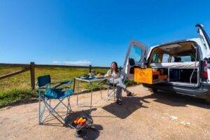 Woman sitting in the open side door of a campervan at a campsite