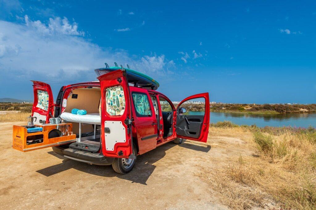 Ocean Camper Vagabond campervan parked by a lagoon in Algarve with surfboards on the roof and camping setup in the back.