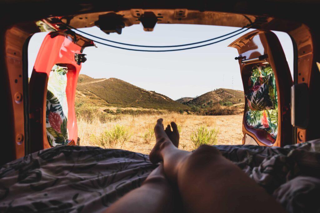 Relaxing inside a campervan with doors open overlooking rural hills in Portugal during a camping road trip.