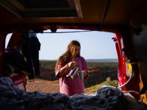 Woman sitting at the back of a campervan watching the sunset, solo travel freedom in Algarve, Portugal.