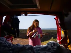 Egy nő egy campervan hátsó részén ülve nézi a naplementét, az egyedül utazás szabadsága az algarvei partvidéken, Portugáliában.