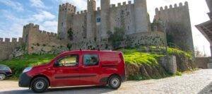 Red campervan parked beside a hilltop castle at dusk