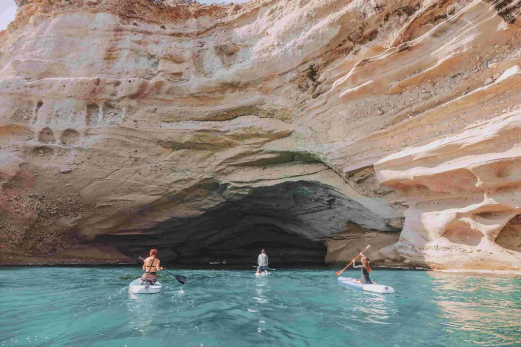People paddleboarding inside a sea cave in Portugal with turquoise water and sunlight shining through the cave entrance.