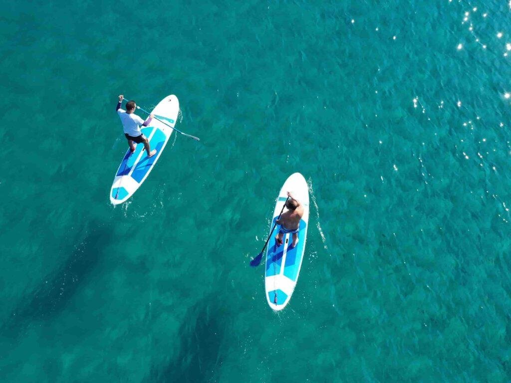 Two people paddleboarding on crystal-clear waters in Algarve, Portugal, enjoying Ocean Camper’s SUP rental experience.