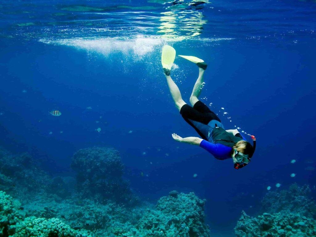 Person snorkeling in clear blue water in Portugal, exploring marine life, Ocean Camper adventure activity.