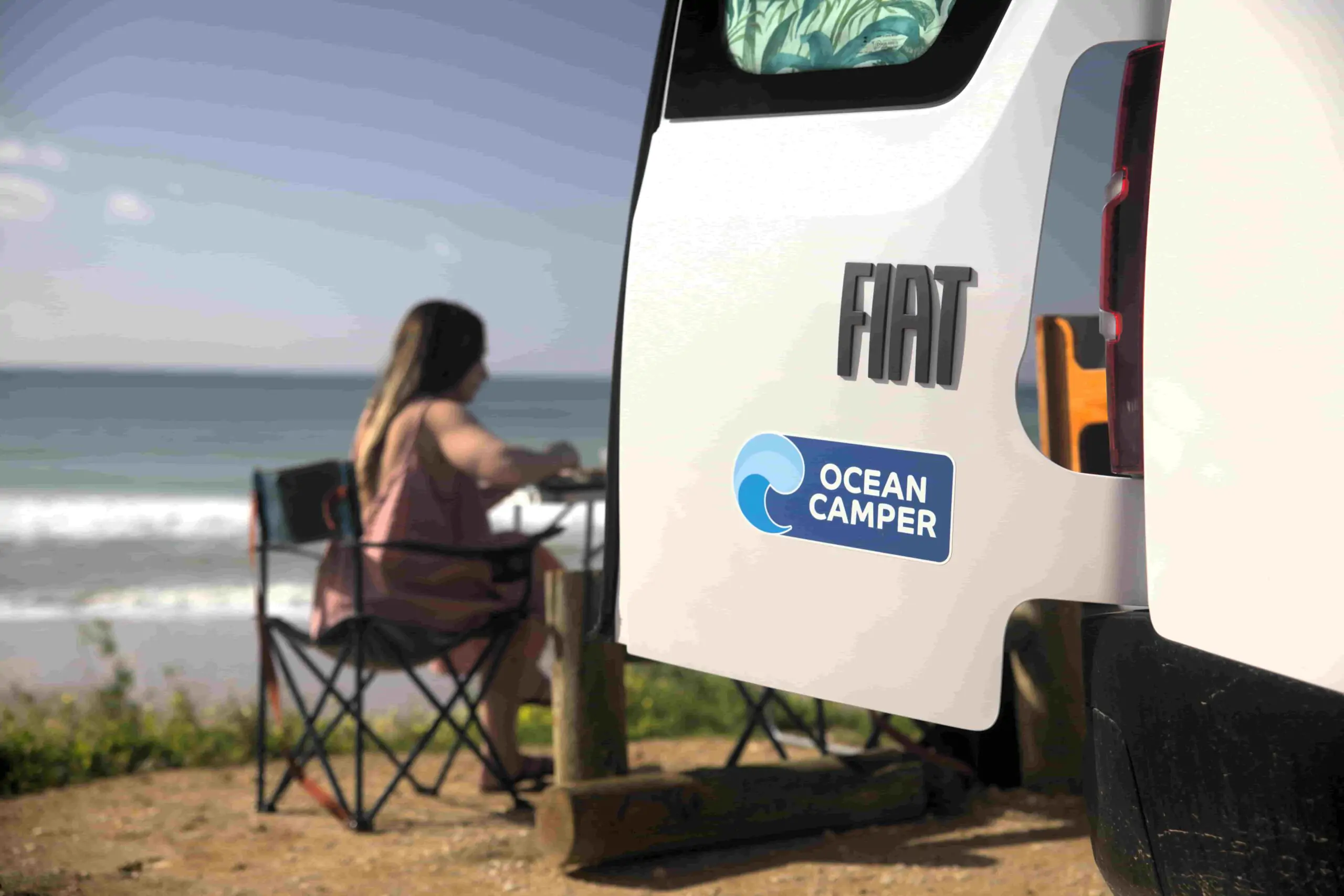 Una camper Ocean aparcada junto a la playa en Portugal, con un viajero relajándose al aire libre y disfrutando de una experiencia en camper sin conexión a la red eléctrica.
