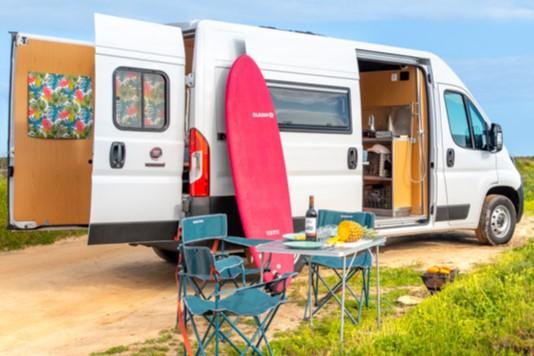 Ocean Camper Bohemian campervan parked by the coast in Algarve with surfboard and camping setup.