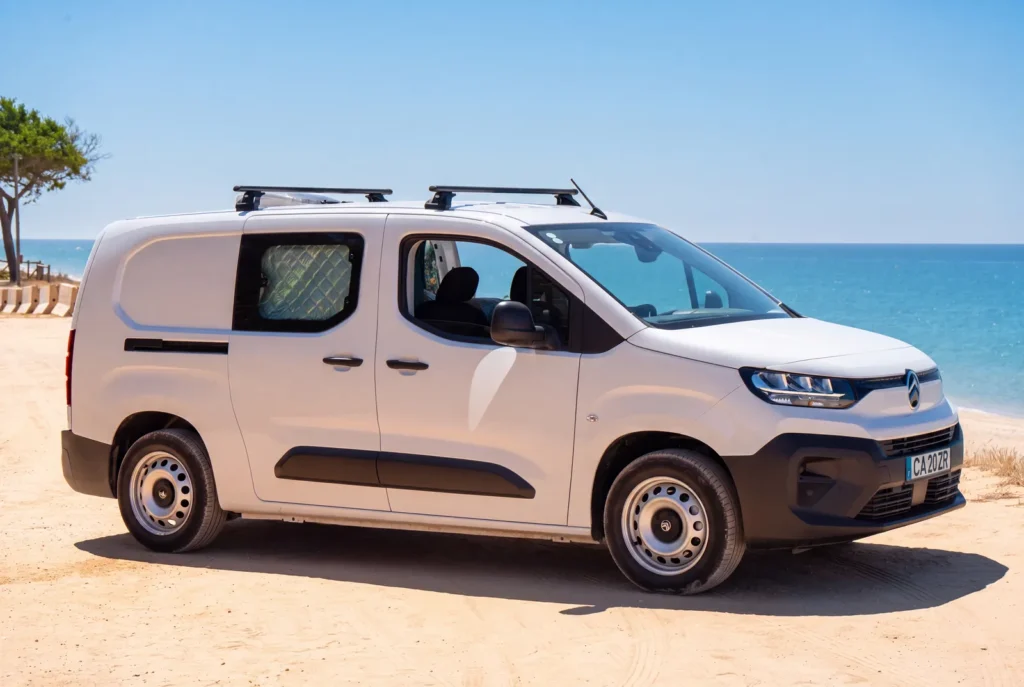 Weißer Citroën Berlingo Campervan mit Dachträger, geparkt im Sand am Meer