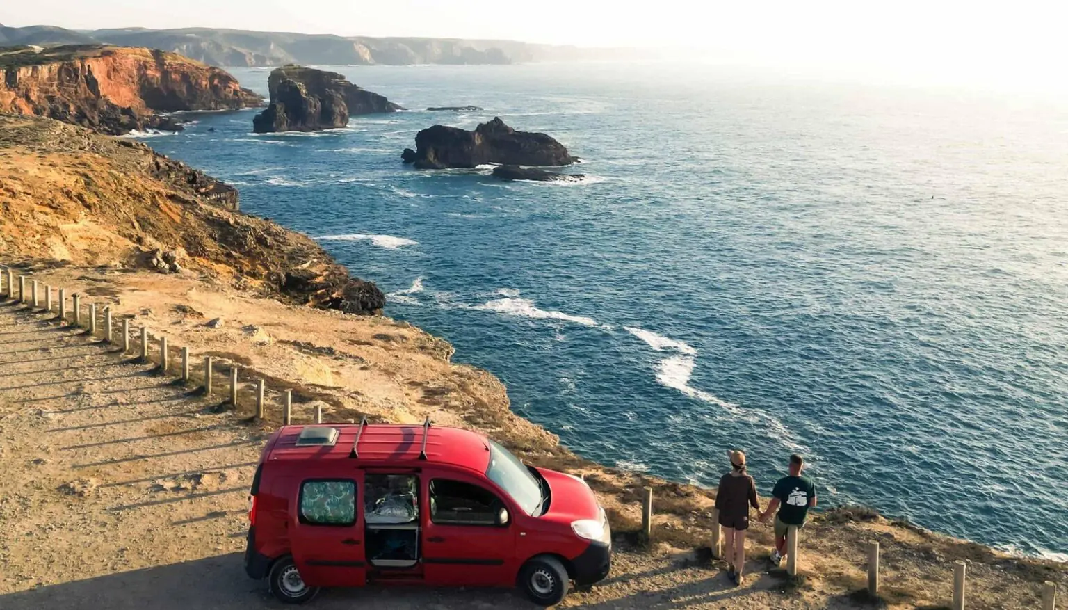 Couple next to a red Ocean Camper campervan on the Algarve cliffs above the Atlantic