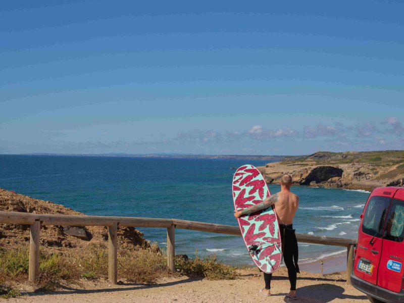Surfer with board next to a mini campervan in Portugal overlooking the ocean