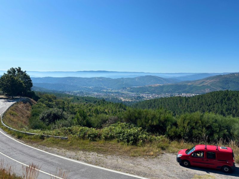 Camper rosso parcheggiato su una strada di montagna con vista panoramica sulle valli e le foreste portoghesi in una giornata di sole.