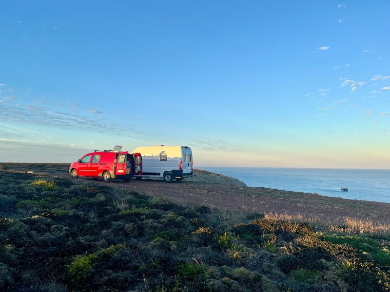 Mini campervan Portugal parked beside a larger campervan on a coastal cliff during sunset, showing the difference between small and big campervans.