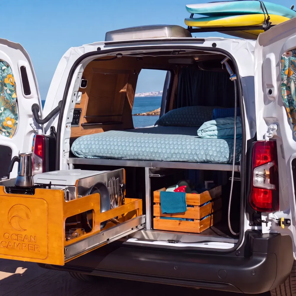 Campervan s otevřenými zadními a bočními dveřmi ukazující postel a výsuvnou kuchyňku