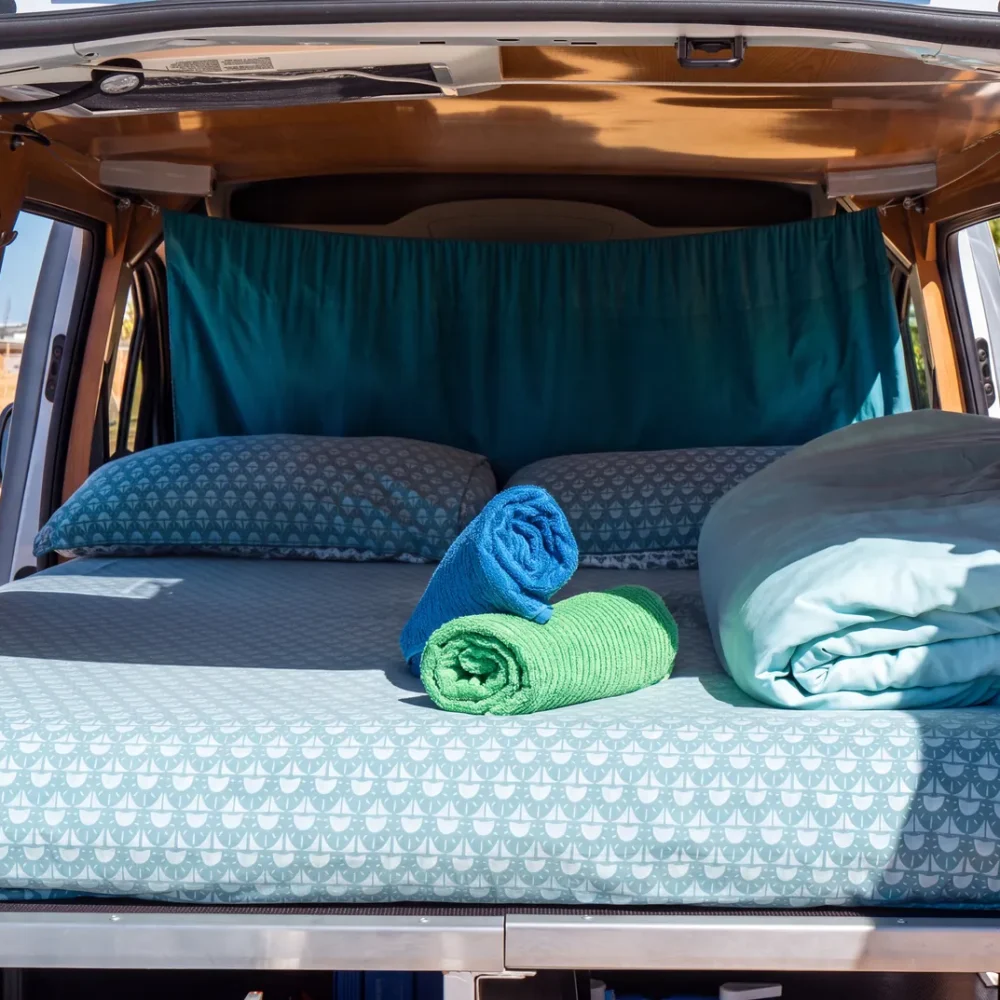 Ustlaná manželská postel s polštáři a složenými ručníky uvnitř campervanu