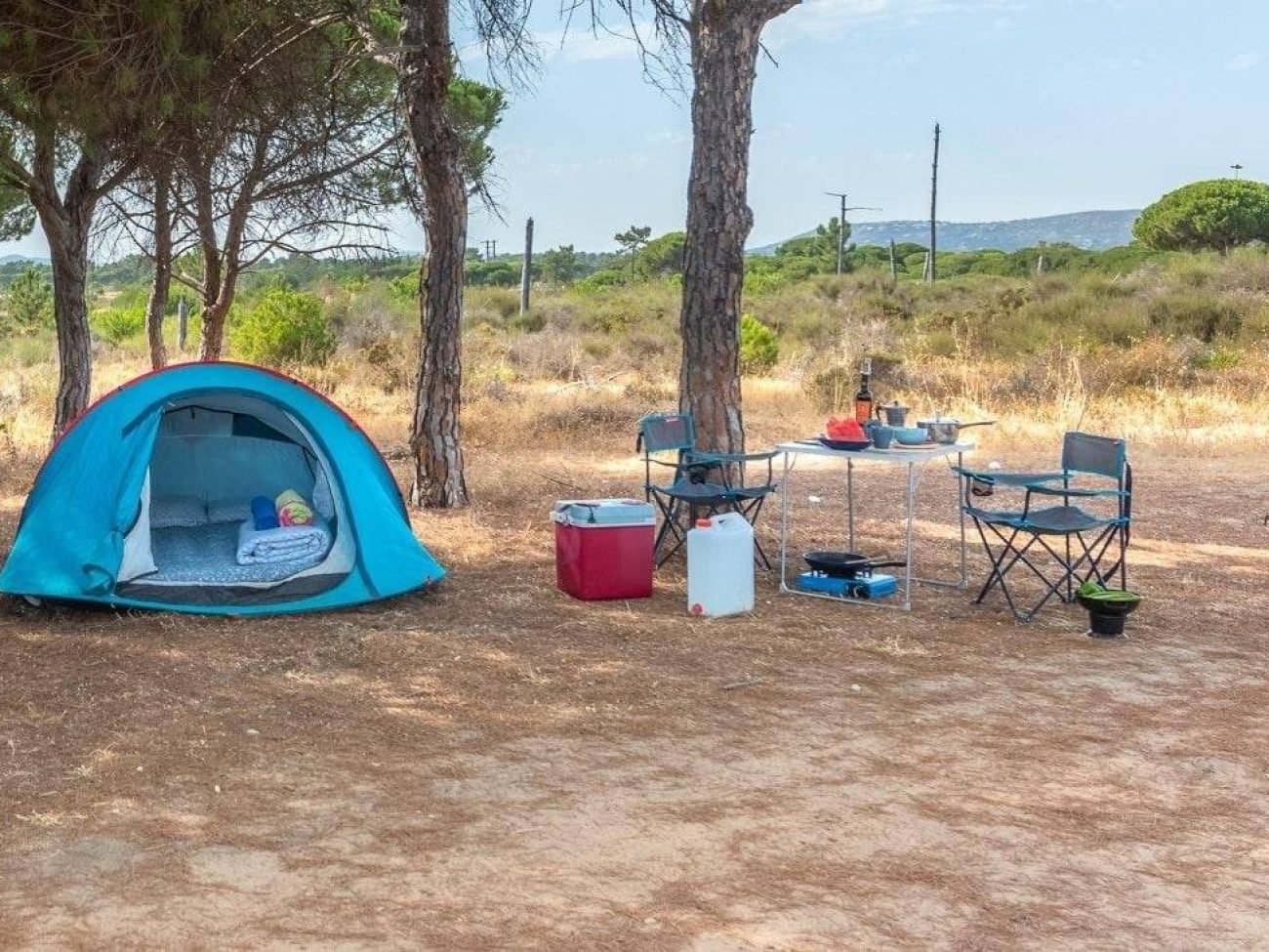 Blue camping tent with table, chairs and camping gear among pine trees, tent rental in Faro