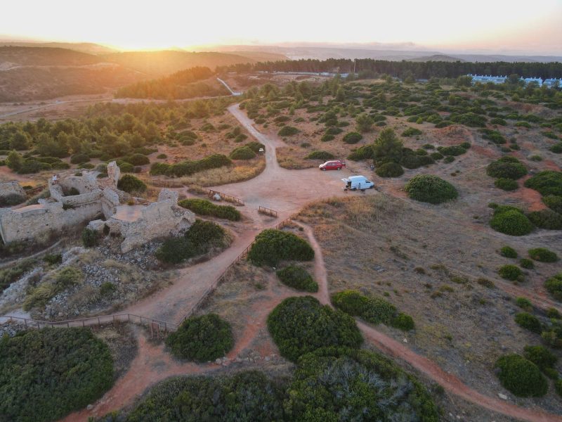 Aerial view of campervans parked on a clifftop at sunset, illustrating wild camping Portugal scenery.