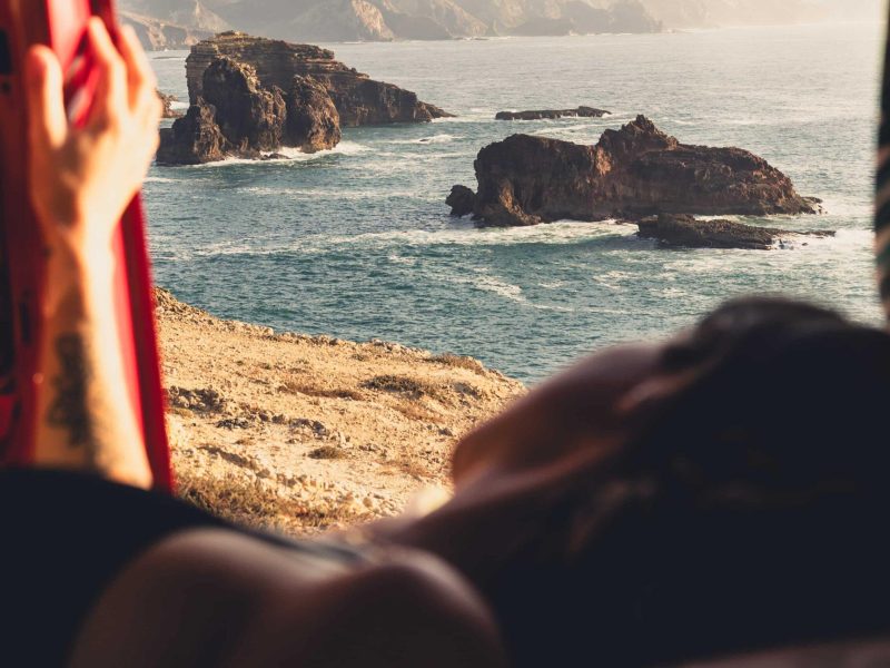 Relaxing inside a campervan with an ocean cliff view during a wild camping Portugal road trip.